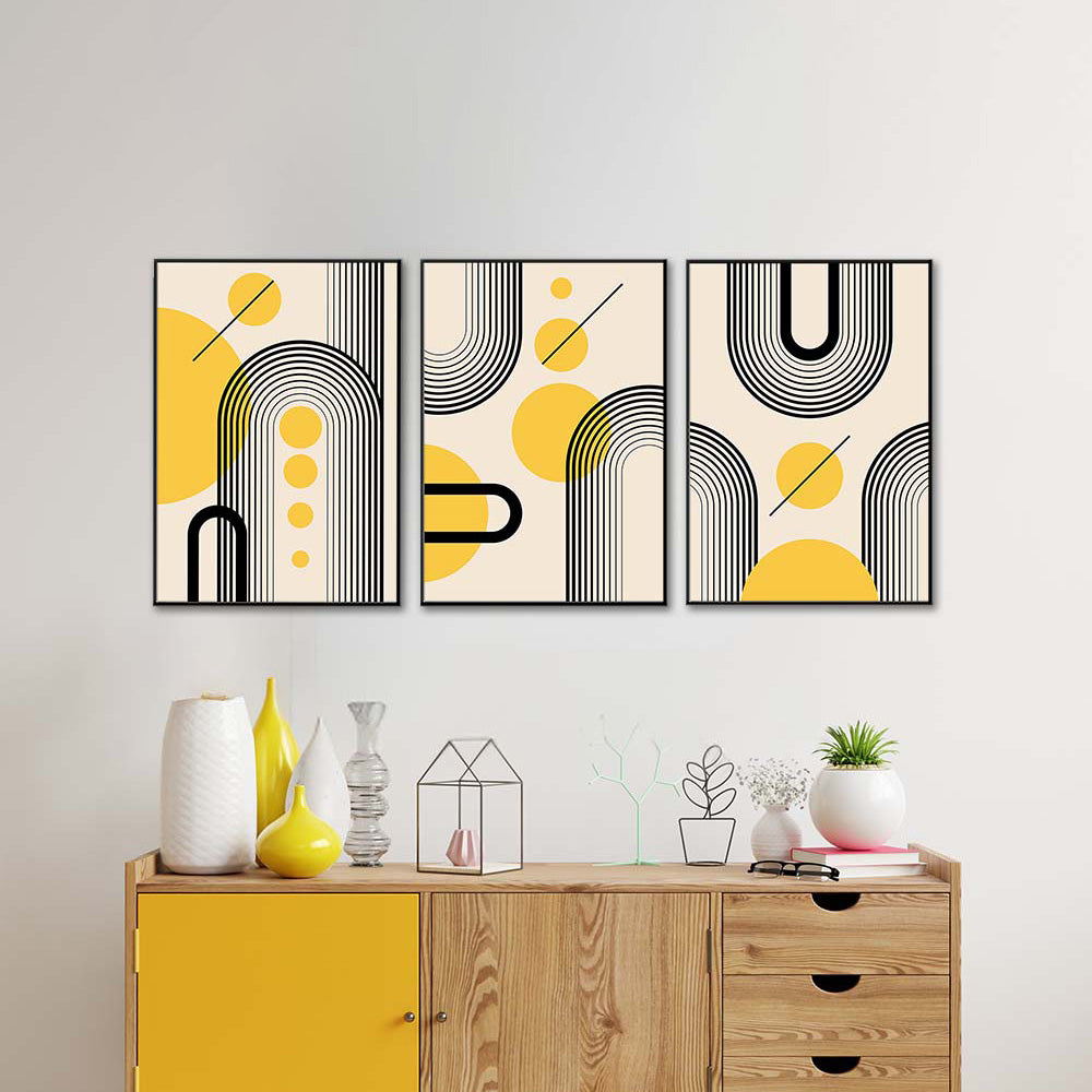 Tris di quadri appesi in fila sopra una madia: archi a righe nere e cerchi gialli su fondo beige, mood retrò.