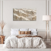 Quadro materico beige con rilievi a strati effetto montagne, appeso centrato sopra letto in camera da letto neutra con lampada e cuscini chiari.