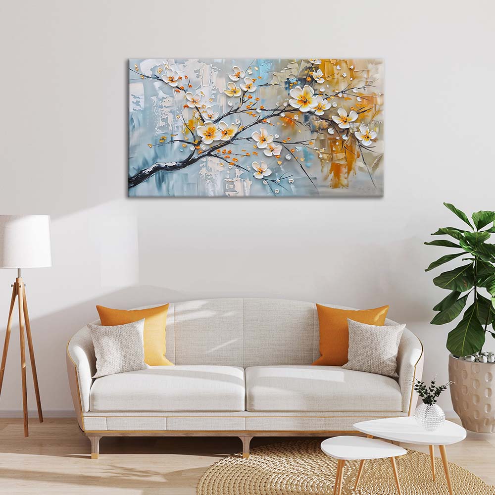 Quadro materico con fiori bianchi a rilievo e tocchi oro su sfondo azzurro e ocra, appeso sopra divano chiaro in soggiorno con cuscini gialli.