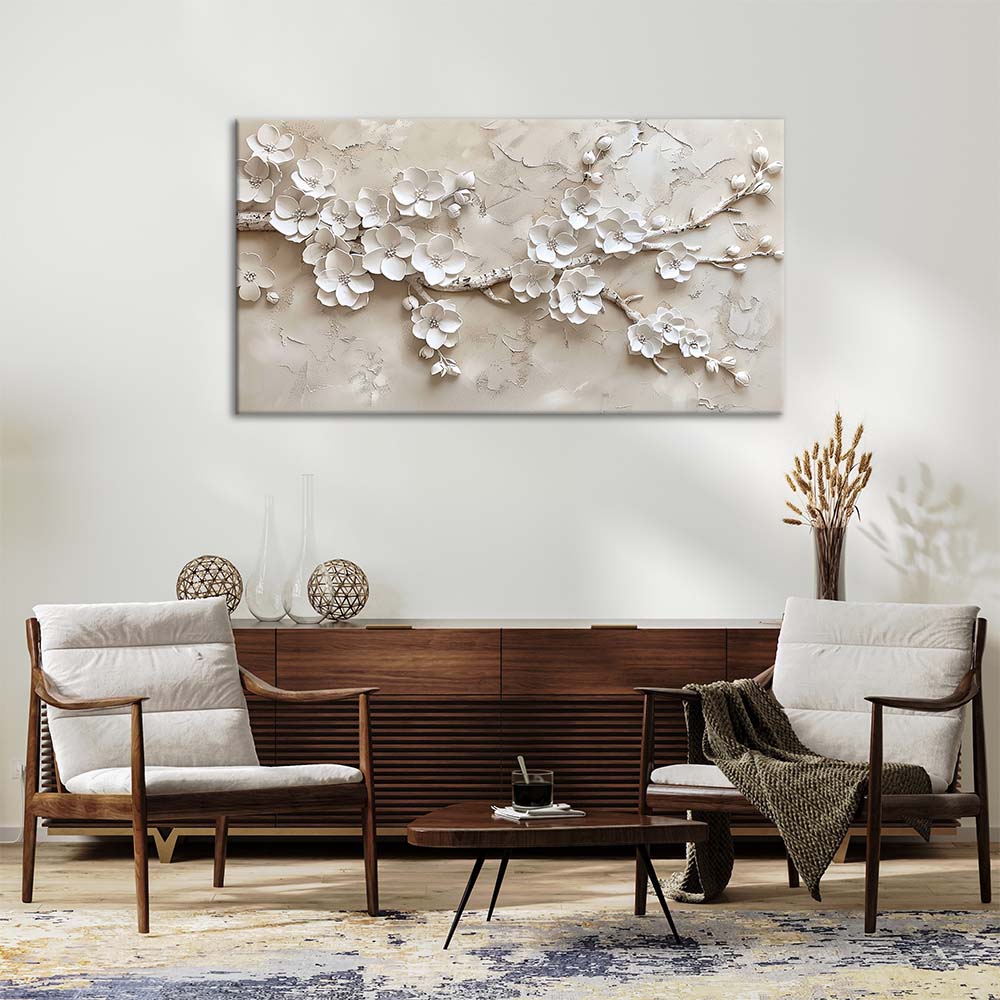 Quadro materico beige con ramo e fiori bianchi in rilievo, appeso su parete chiara sopra credenza in legno in soggiorno con poltrone e tavolino.