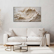 Quadro materico con onda crema in rilievo, appeso centrato sopra divano bianco in soggiorno luminoso con tavolini rotondi e parete grigio chiaro.