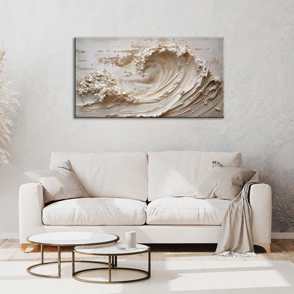 Quadro materico con onda crema in rilievo, appeso centrato sopra divano bianco in soggiorno luminoso con tavolini rotondi e parete grigio chiaro.
