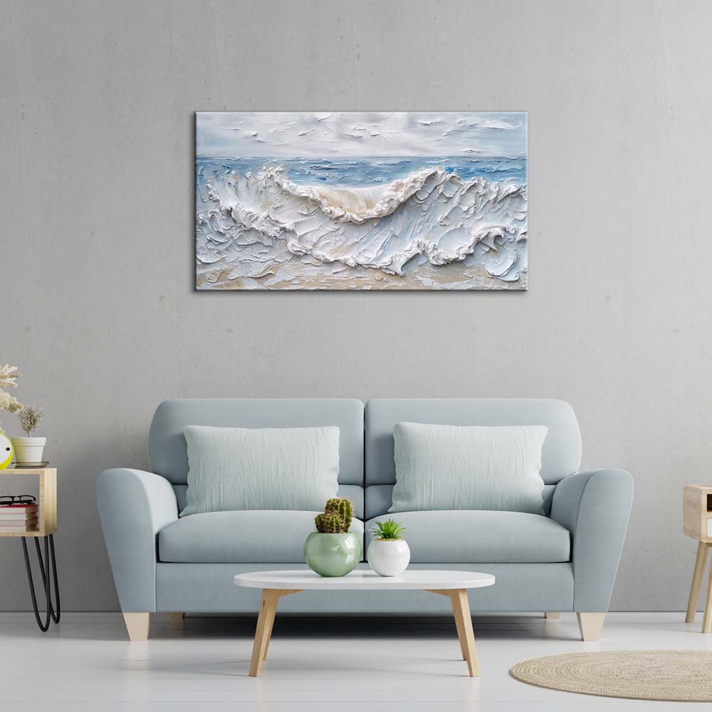 Quadro materico con onda bianca in rilievo e mare azzurro, appeso centrato sopra divano celeste su parete grigia, tavolino bianco con piante.