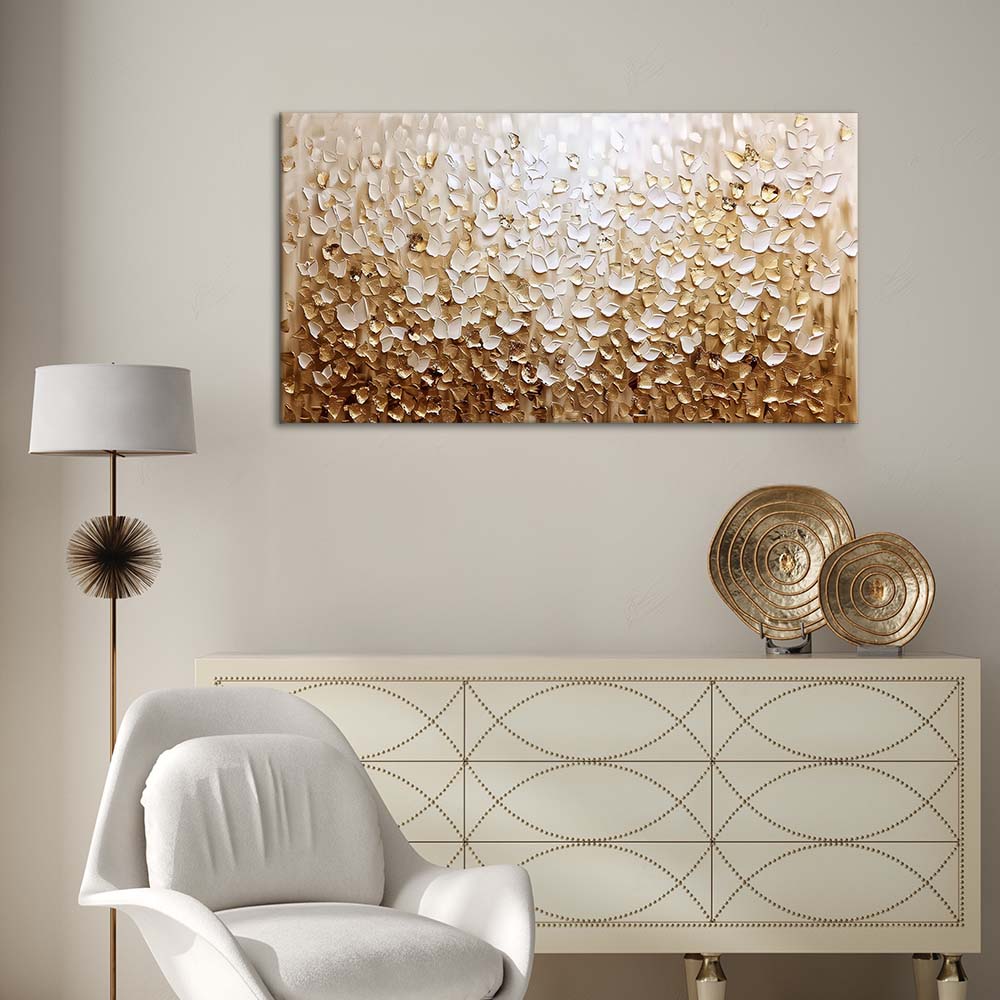 Quadro materico astratto con petali bianchi e oro appeso in soggiorno, sopra credenza chiara con lampada e decorazioni dorate