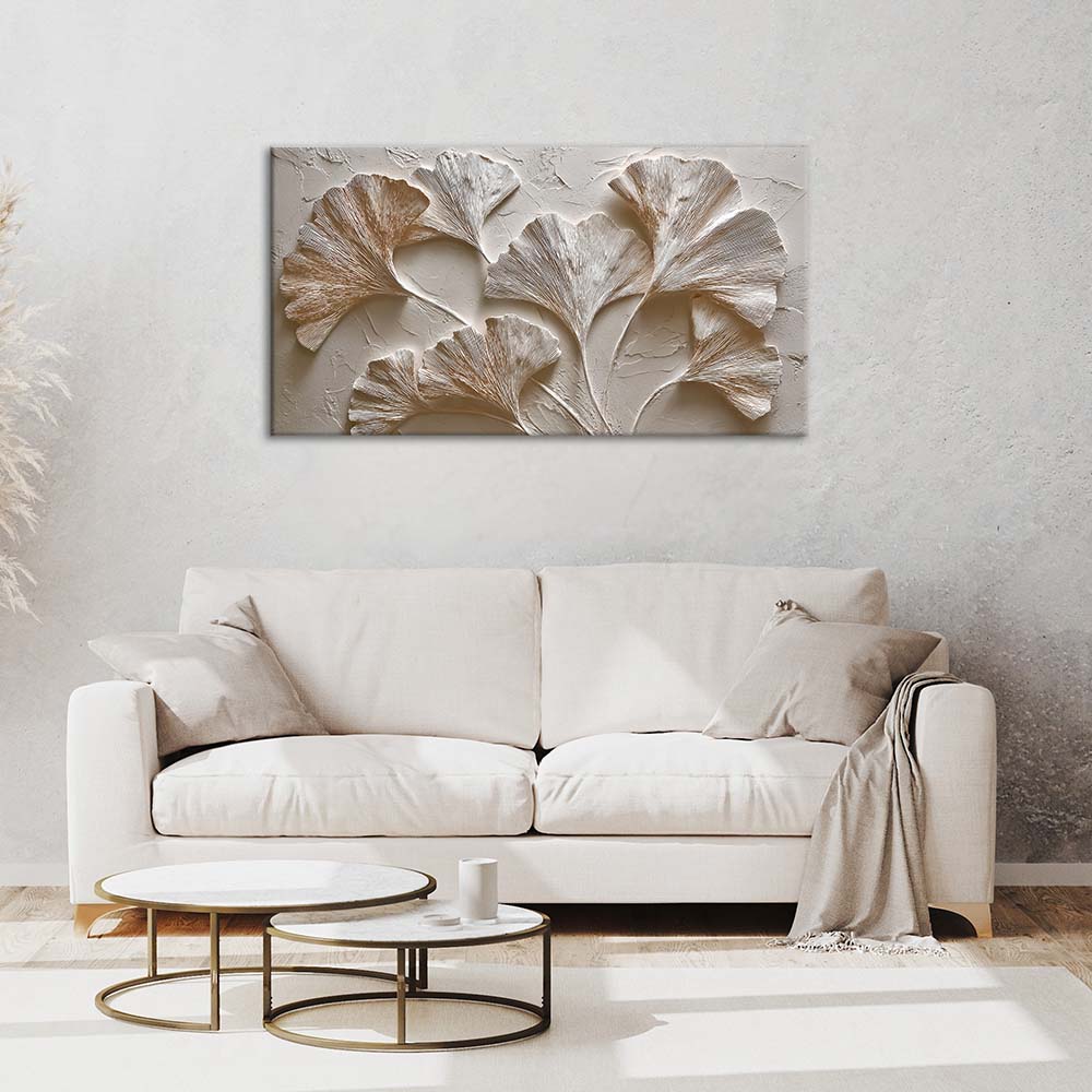 Quadro materico con foglie di ginkgo in rilievo bianco e oro appeso sopra divano chiaro, ambientazione soggiorno minimal.