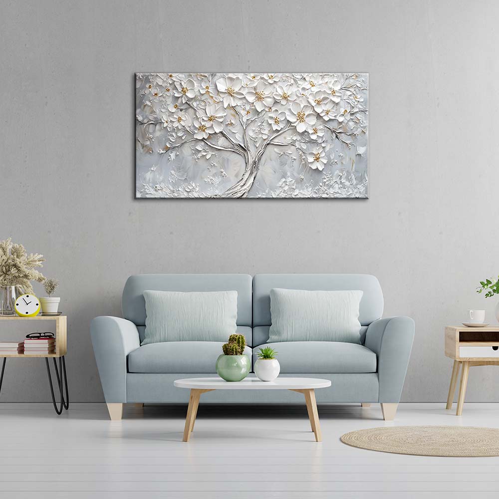 Quadro materico con albero fiorito bianco appeso centrato sopra divano azzurro in soggiorno moderno, fondo grigio con dettagli oro.
