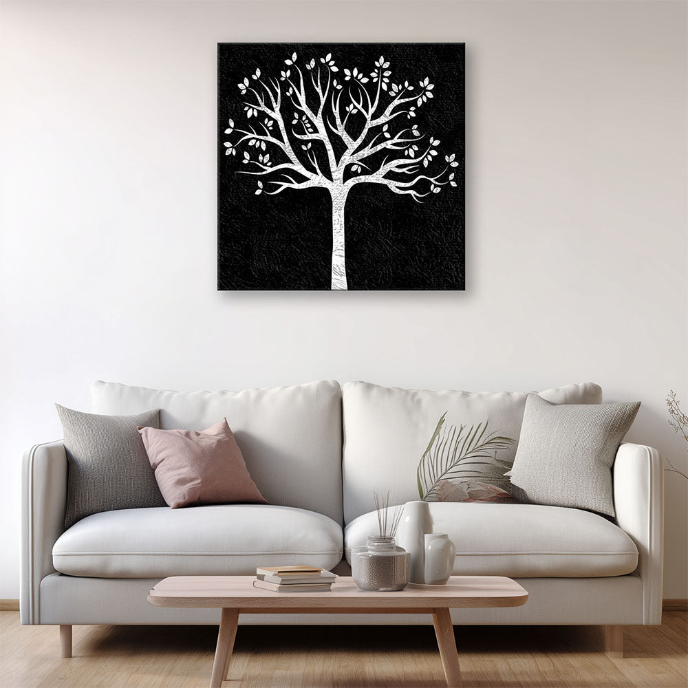 Quadro bianco e nero con albero stilizzato appeso a una parete chiara sopra un divano moderno beige, con cuscini decorativi e tavolino in legno.