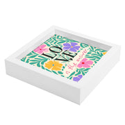 Svuotatasche bianco decorato con testo ispirazionale tra fiori rosa, viola, gialli e foglie verdi, vista laterale.