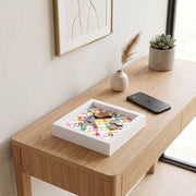 Svuotatasche in legno bianco con decoro geometrico colorato a triangoli, con chiavi, portachiavi in pelle e monete su consolle in legno chiaro