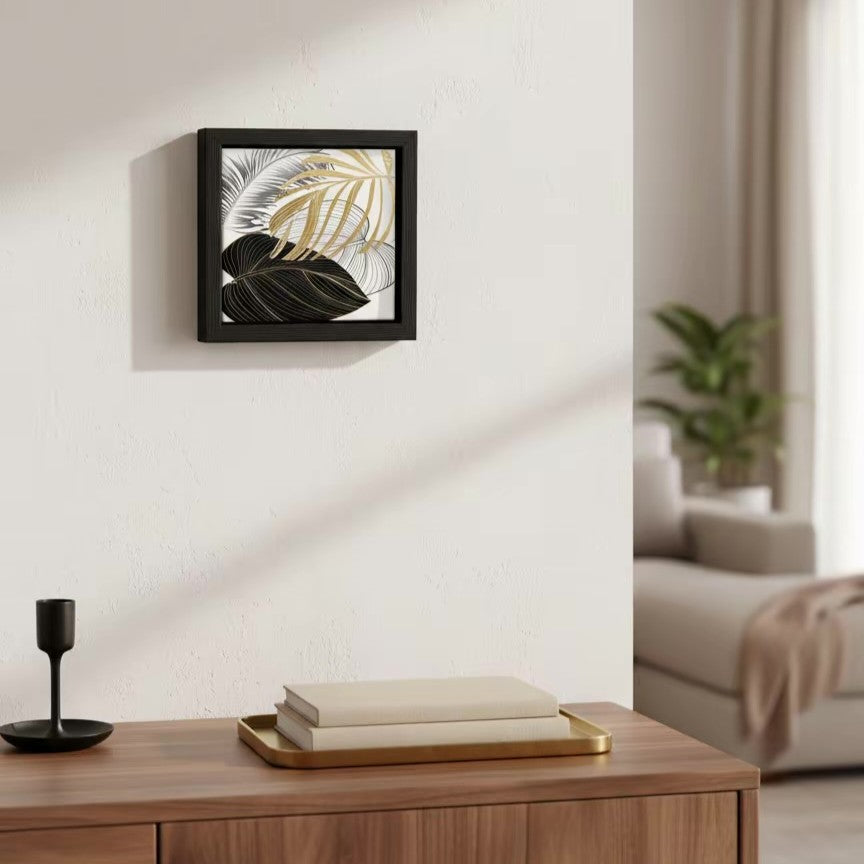quadretto in ceramica decorata con foglie nere e oro e con cornice in legno nera, appeso su una parete bianca in un ingresso moderno