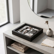 Svuotatasche in legno nero con decoro geometrico a righe grigio e beige, con portachiavi in pelle, orologio e portacarte su consolle in cemento