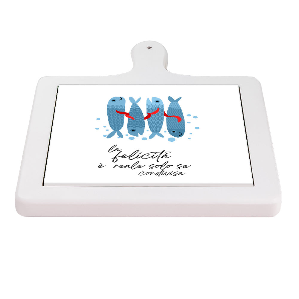 Tagliere orizzontale in ceramica bianca con pesci azzurri, nastri rossi e frase “La felicità è reale solo se condivisa”.