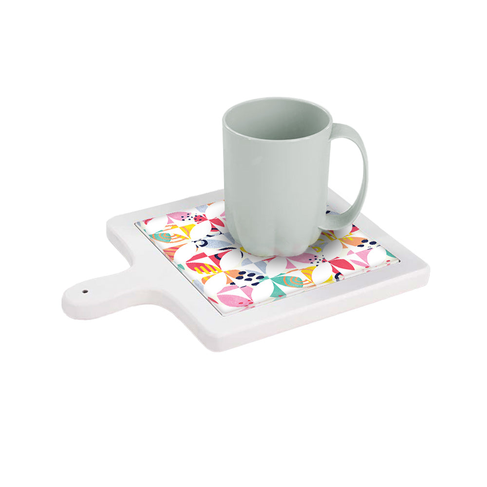 Tagliere in ceramica bianca orizzontale con tazza sopra, decorato con pattern floreale geometrico multicolore su sfondo bianco.