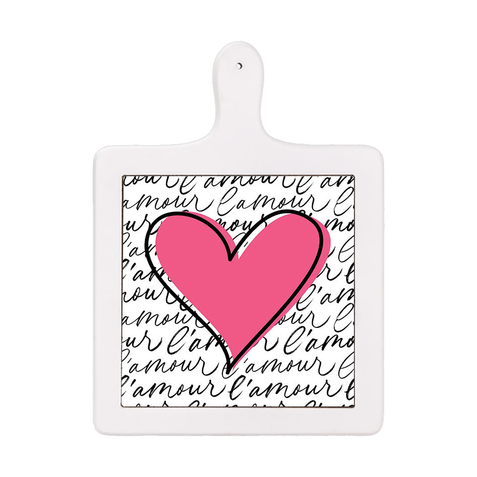 Tagliere verticale in ceramica bianca con cuore rosa acceso e sfondo con scritta “l’amour” nera ripetuta in corsivo su bianco
