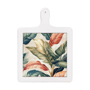 Tagliere verticale in ceramica bianca con design tropicale: grandi foglie verdi, arancioni e beige su fondo chiaro.