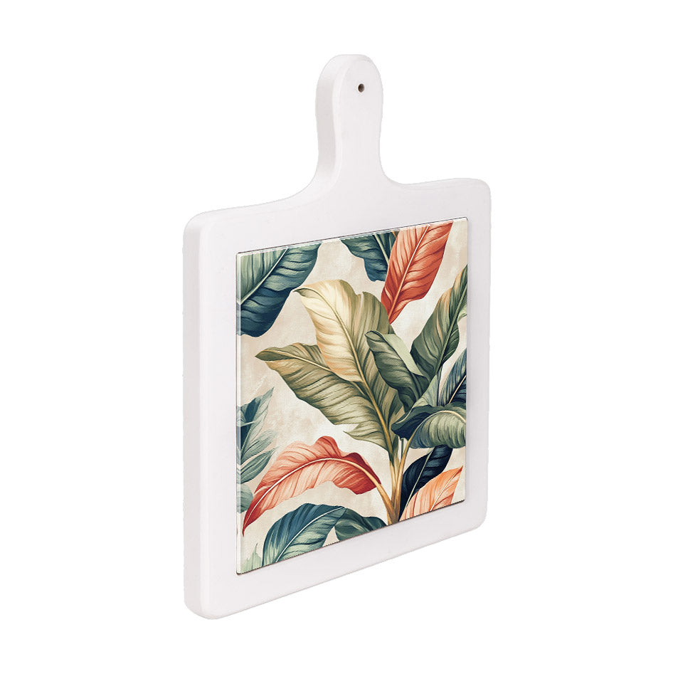 Tagliere verticale in ceramica bianca visto lateralmente, con foglie tropicali verdi, rosse e beige su fondo chiaro.