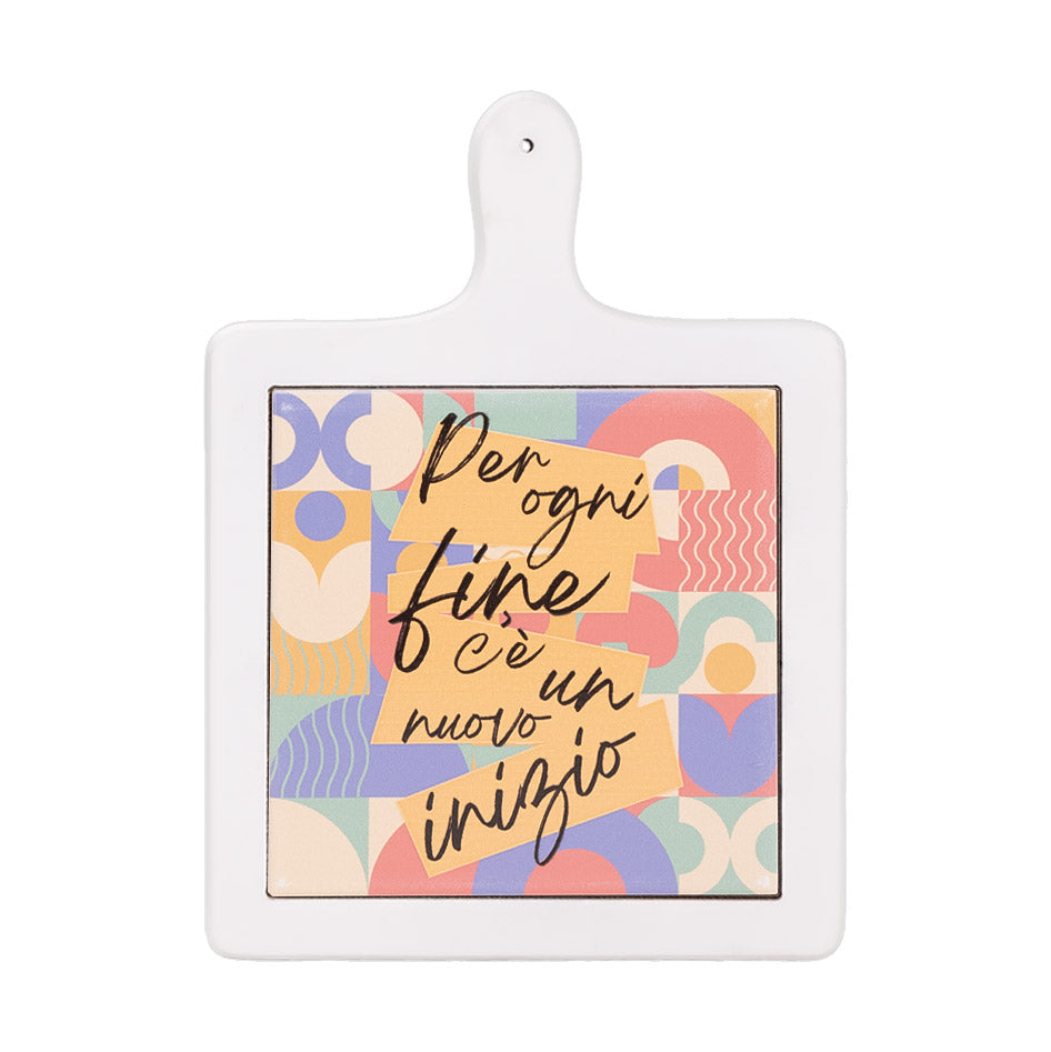 Tagliere in ceramica bianca con motivo astratto colorato e scritta "Per ogni fine c’è un nuovo inizio" al centro.