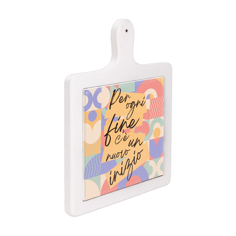 Tagliere verticale in ceramica bianca visto lateralmente, con scritta motivazionale su fondo geometrico colorato.