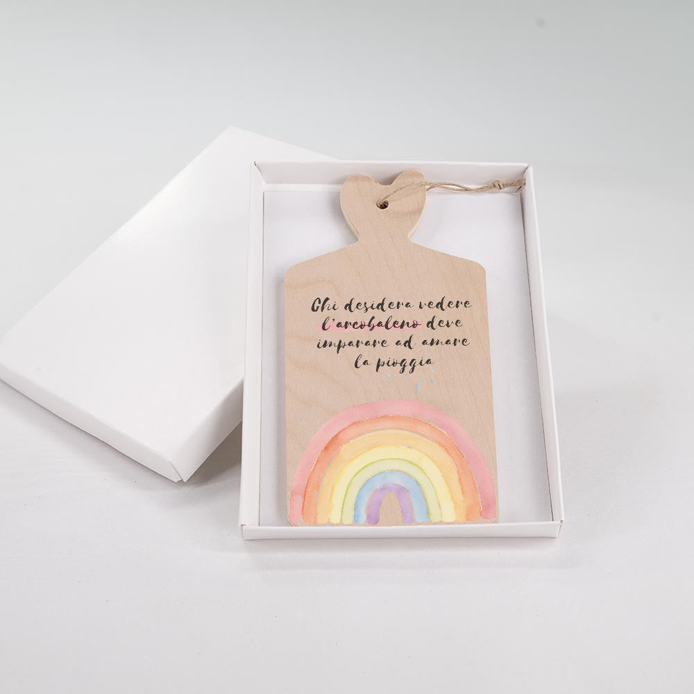 Tagliere in legno con arcobaleno e scritta, in scatola regalo bianca aperta, con manico a cuore e cordino decorativo.