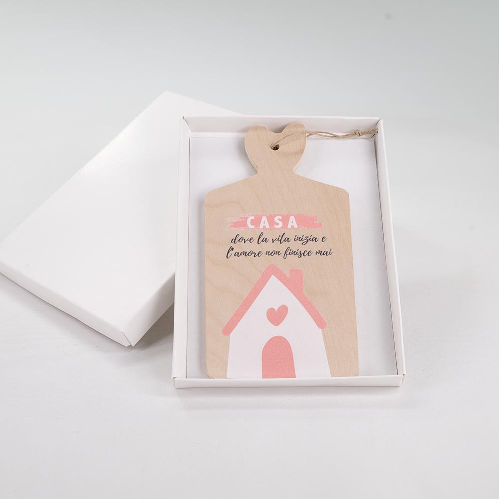 Tagliere in legno con casetta e scritta affettuosa sulla casa, presentato in scatola regalo bianca aperta con manico a cuore.