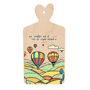 Tagliere in legno con paesaggio di colline variopinte, cielo con mongolfiere colorate e citazione sul sogno, manico sagomato a forma di cuore.