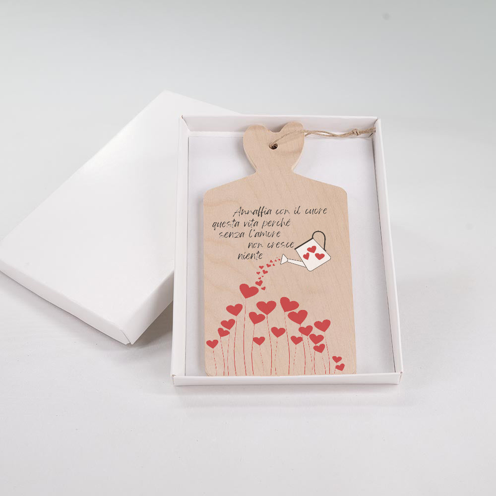 Tagliere in legno con manico a cuore, disegno floreale a cuori e frase motivazionale, presentato in scatola regalo bianca.