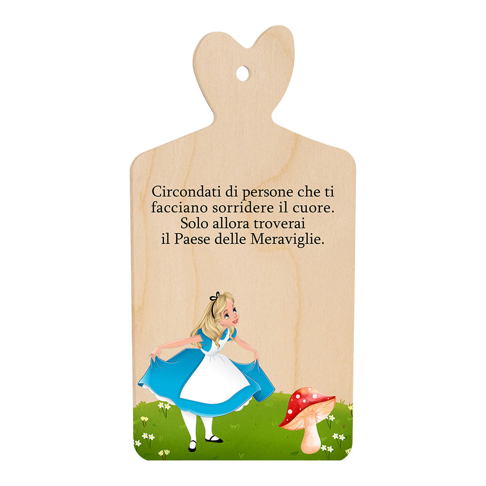Tagliere in legno a forma di cuore con frase incisa e illustrazione di una bambina accanto a un fungo su prato verde.