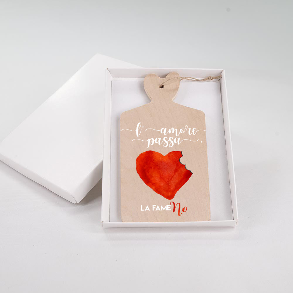 Tagliere in legno con cuore rosso acquerello morso e scritta "L'amore passa, la fame no" in bianco e rosso, in scatola regalo bianca.