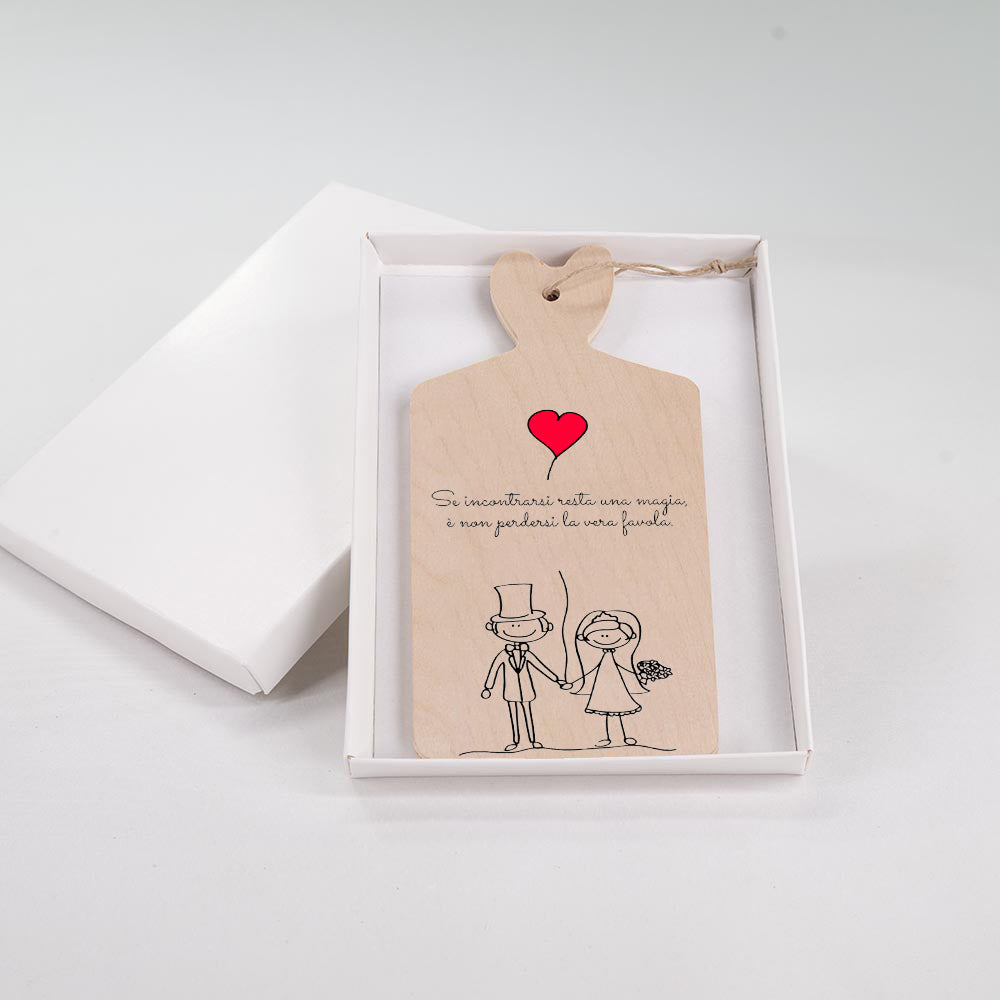 Tagliere in legno con illustrazione di sposi lineari che si tengono per mano, cuore rosso e frase romantica sul matrimonio, in scatola bianca.