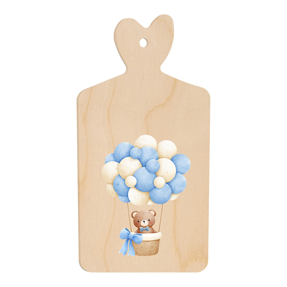 Tagliere in legno a forma di cuore con illustrazione di un orsetto in mongolfiera fatta di palloncini azzurri e bianchi, in stile dolce e infantile.