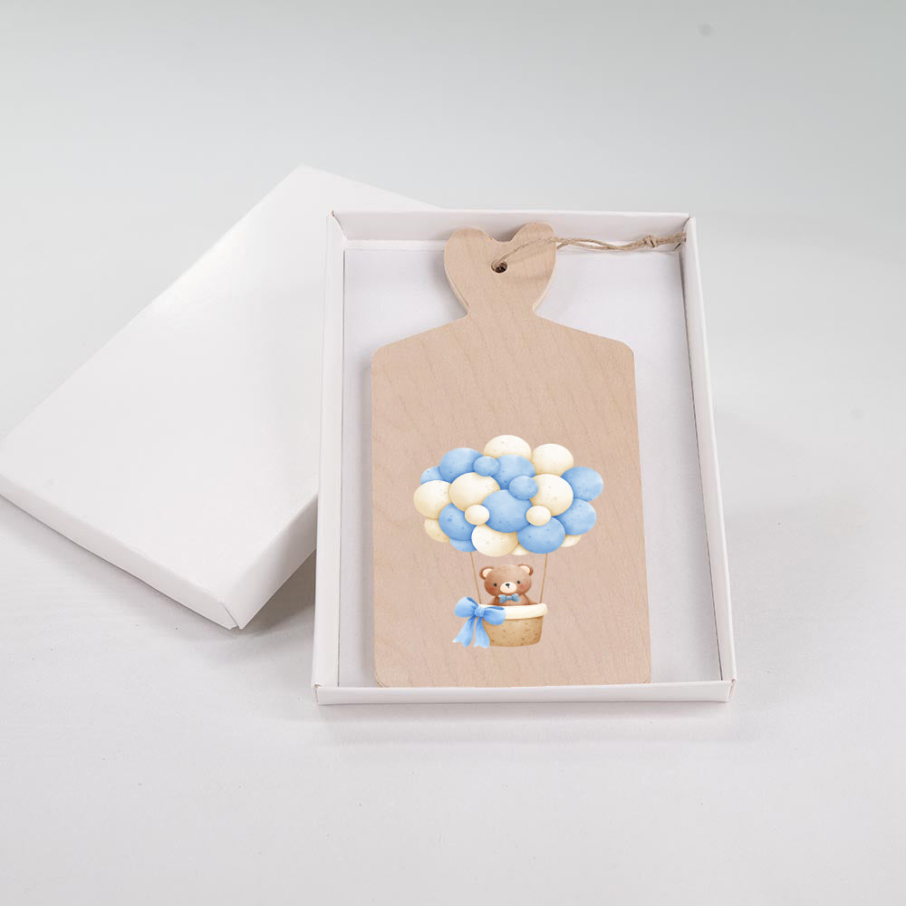 Tagliere in legno con orsetto in mongolfiera di palloncini azzurri e bianchi con fiocco celeste, in scatola bianca.
