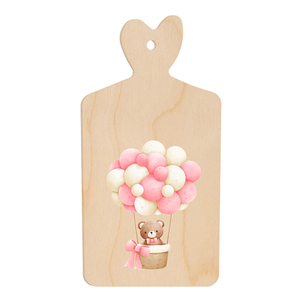 Tagliere in legno a forma di cuore con illustrazione di un orsetto in mongolfiera fatta di palloncini rosa e bianchi, in stile dolce e infantile.