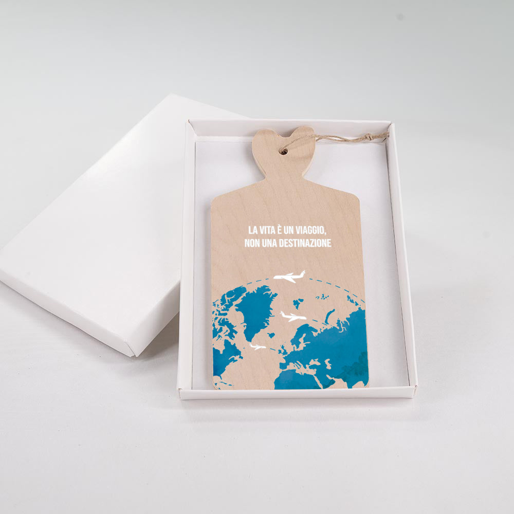 Tagliere in legno con mappa del mondo in blu e aerei bianchi in volo, frase "La vita è un viaggio, non una destinazione", in scatola bianca.
