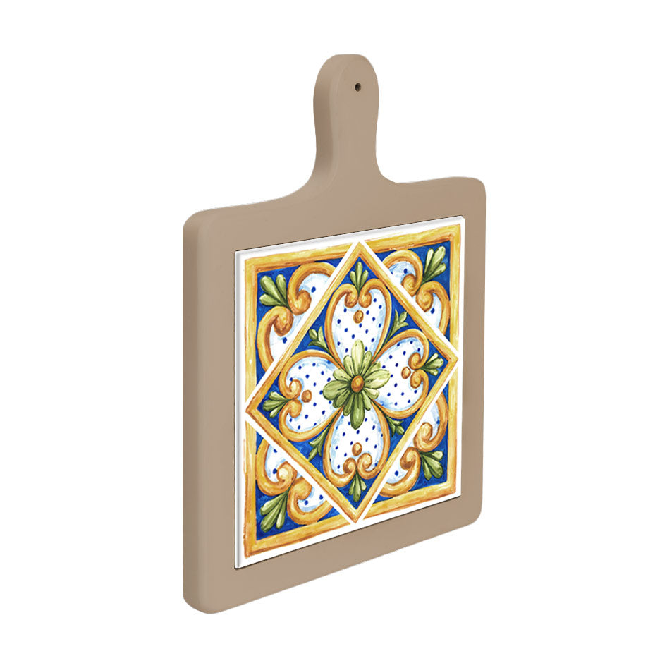 Tagliere in ceramica beige appeso verticalmente, piastrella decorativa centrale con fiore verde, riccioli dorati e fondo blu puntinato.